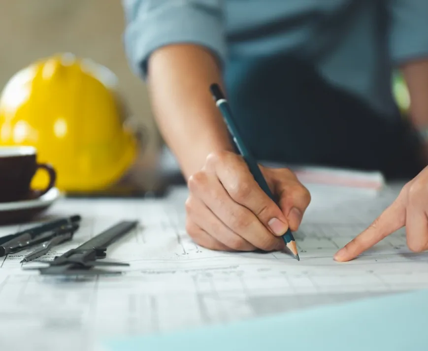 Engineer marking up structural drawings at a desk beside a hard hat