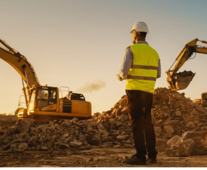 Site engineer in hi-vis on a construction site at sunset with excavators behind